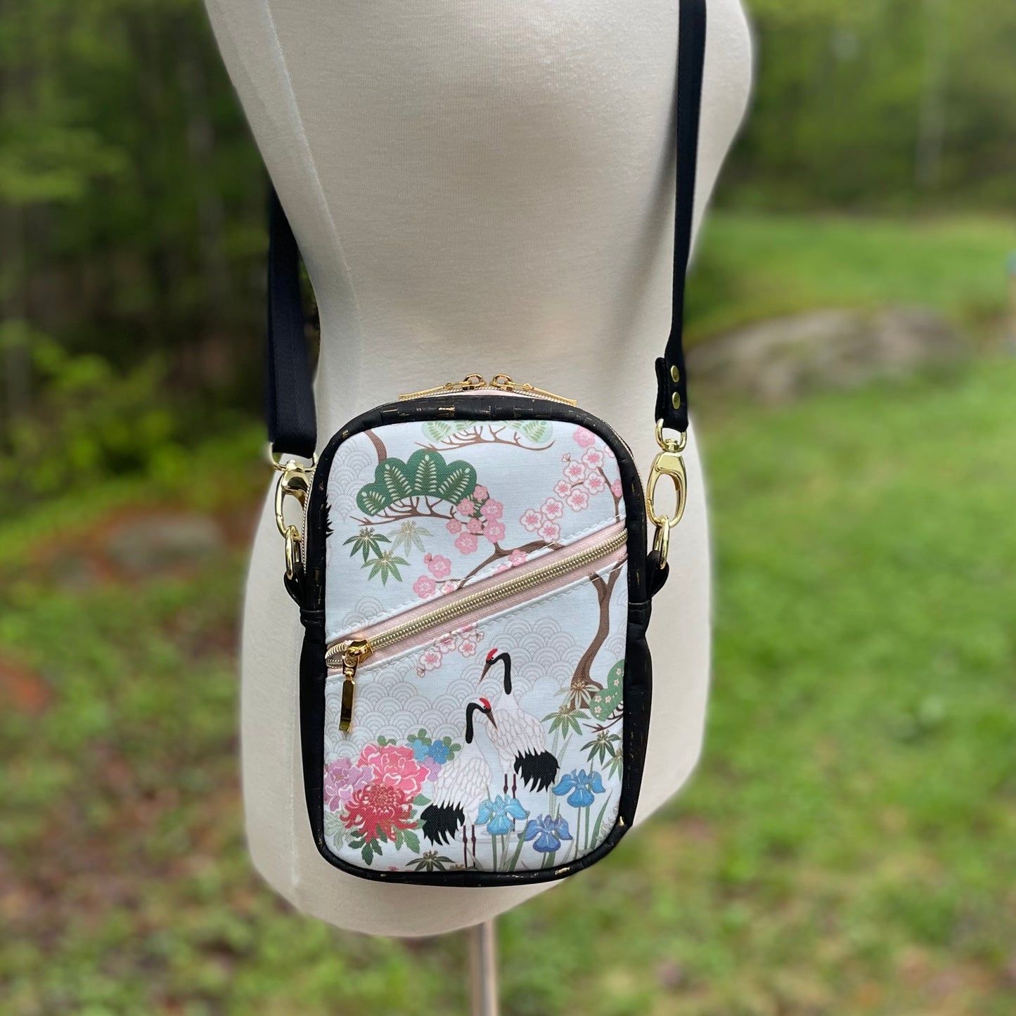 Sac bandoulière en liège noir et doré au devant en canevas vert à motif de fleurs et de grues de style asiatique.