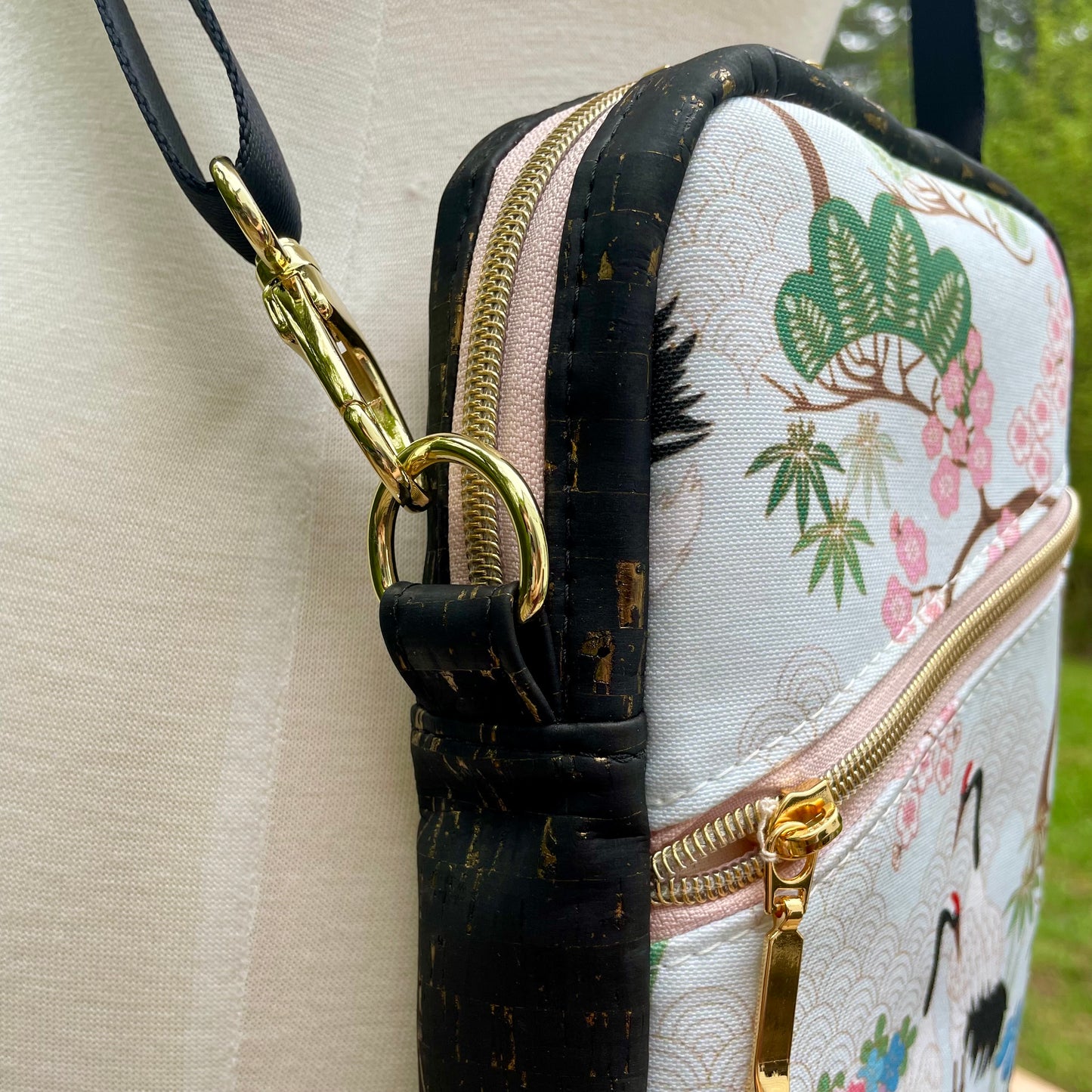 Sac bandoulière en liège noir et doré au devant en canevas vert à motif de fleurs et de grues de style asiatique.